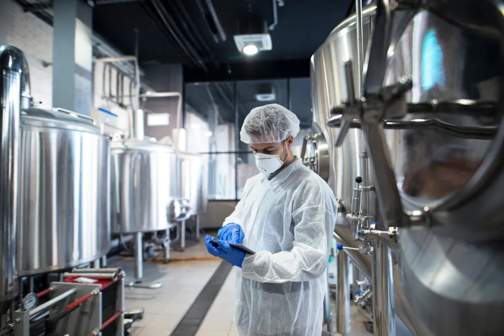 Laboratory technician in protective gear inspecting equipment in a pharmaceutical manufacturing facility, emphasizing Agere Sciences' commitment to high-quality APIs and research compounds.